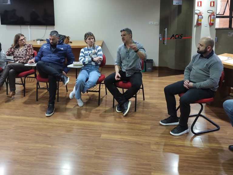 Participantes da Reunião da Comissão de Segurança sentados na sala da ACIS, com a porta de vidro da entidade ao fundo